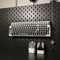 Mechanical keyboard on a black pegboard with tools below
