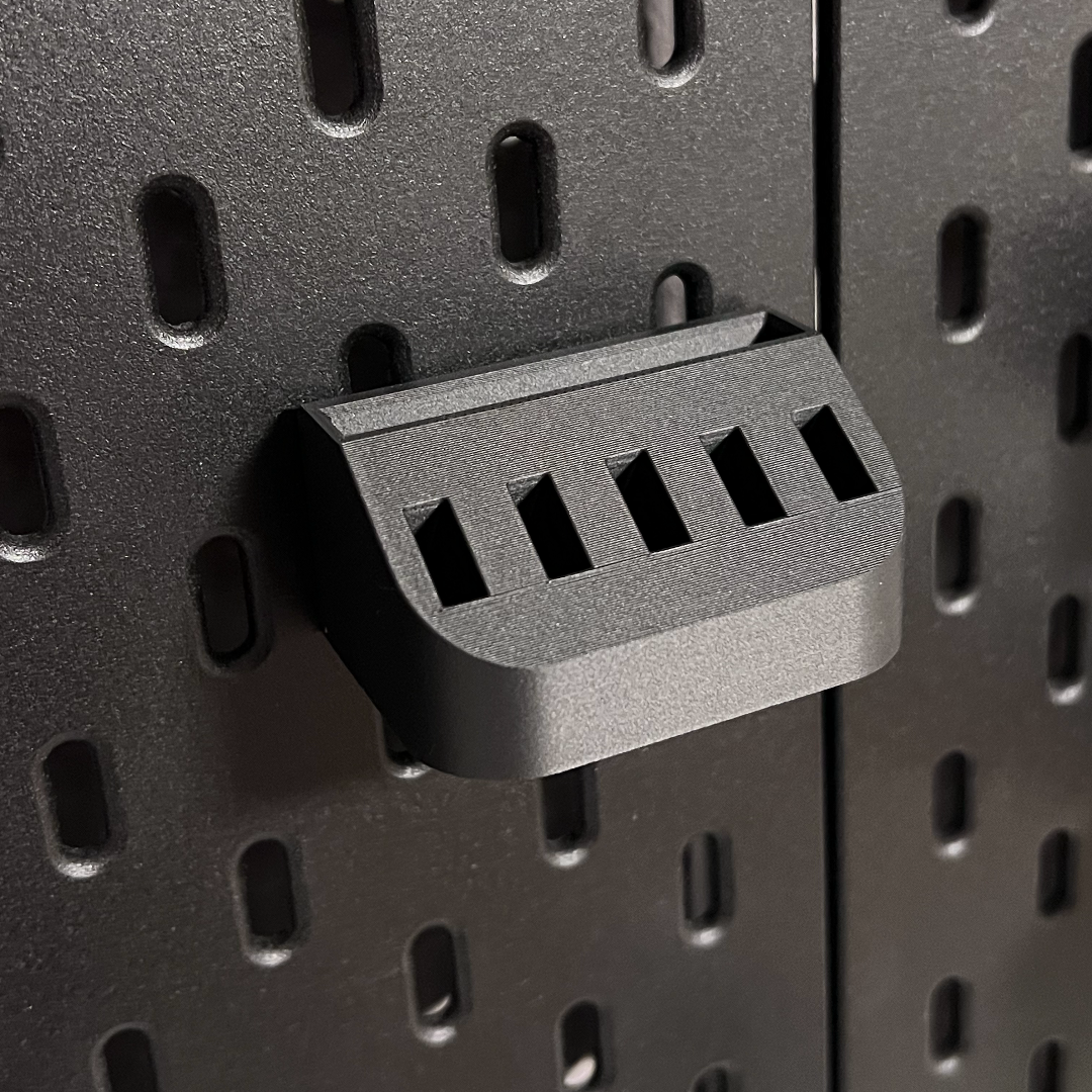 Close-up of a black pegboard bracket on a perforated black pegboard.