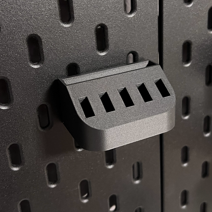 Close-up of a black pegboard bracket on a perforated black pegboard.